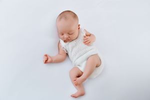Sleeping baby in white onesie lying on white backdrop during newborn photography session.