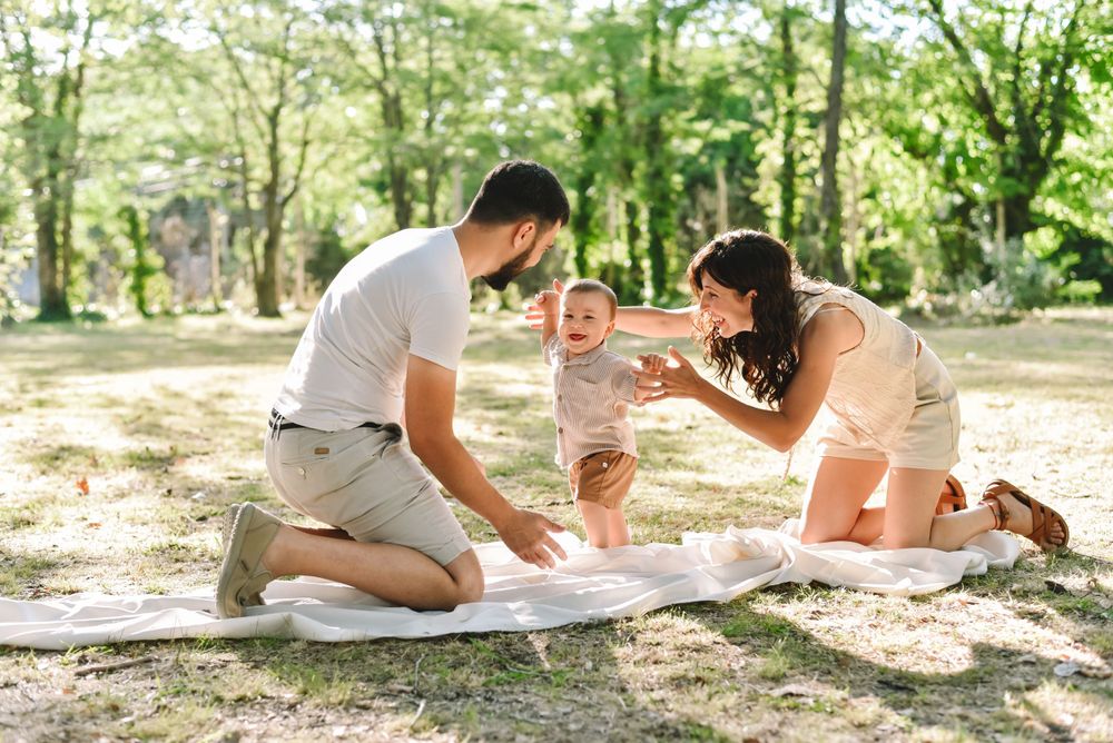 A family spends quality time together outdoors on a blanket in a sun-dappled wooded area.
