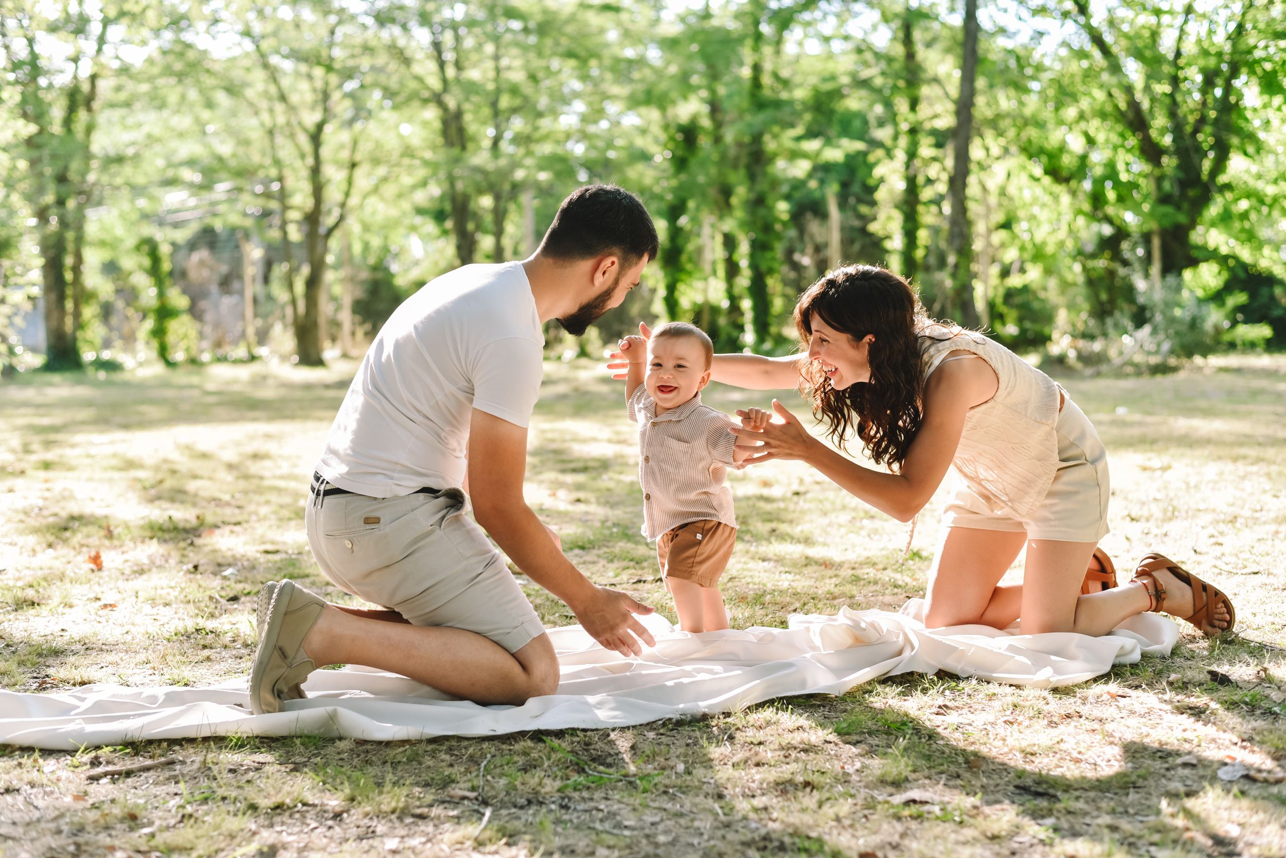 A family spends quality time together outdoors on a blanket in a sun-dappled wooded area.