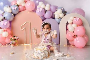 Pink and purple balloon garland with floral accents for first birthday celebration.