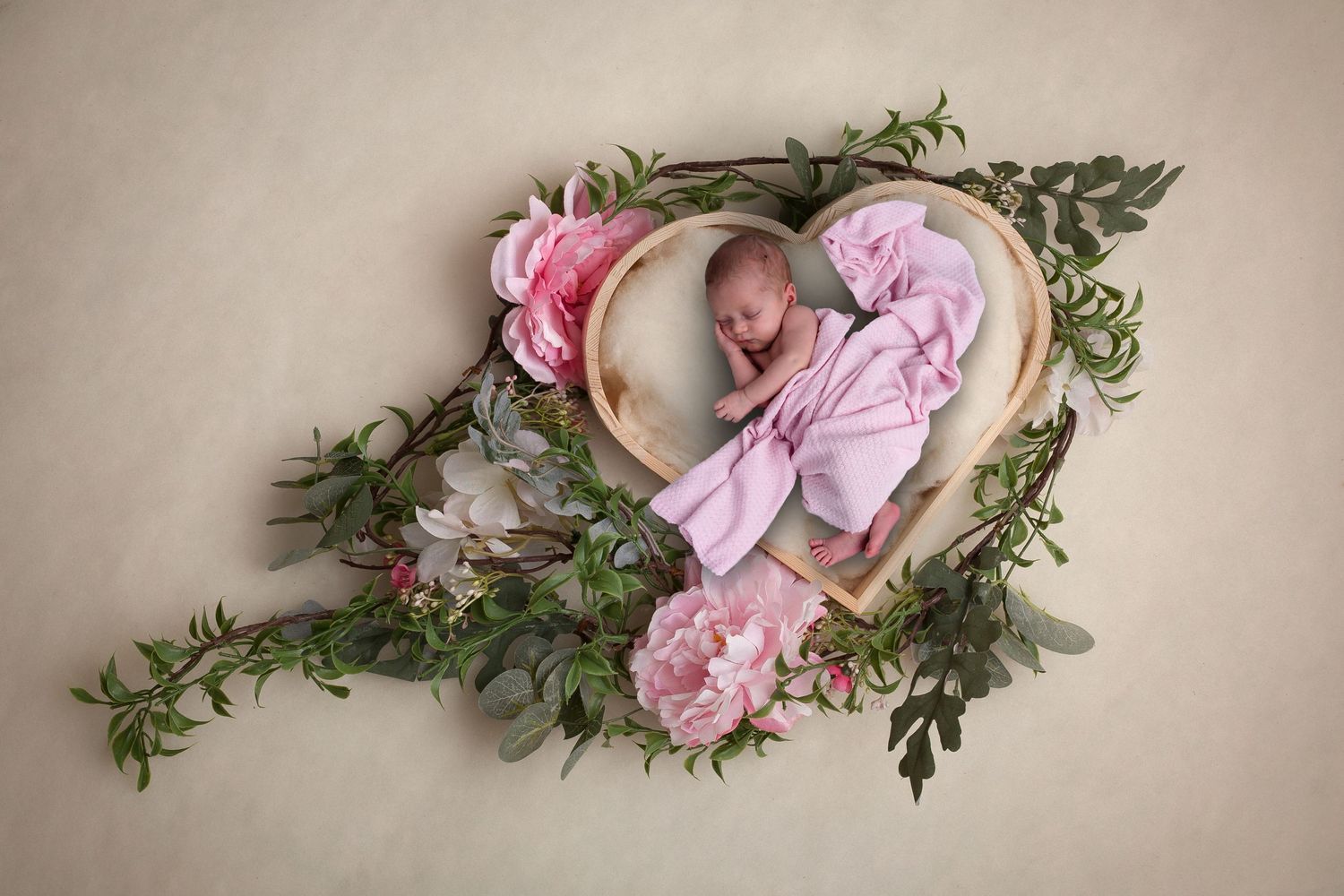 Creative newborn photography with heart-shaped floral frame and pink accents.