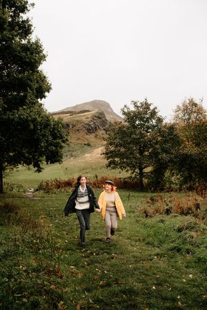 Two people walk along a grassy hillside path on an autumn day with rolling hills in the background.