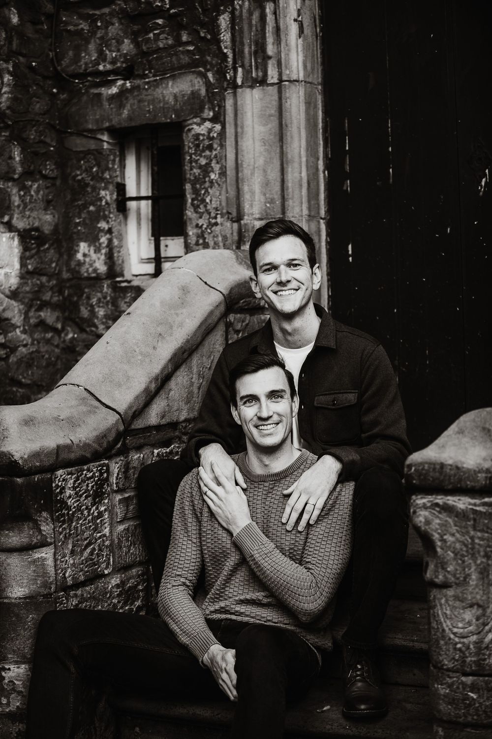 Two people share joyful moments together while sitting on stone steps of an old building.