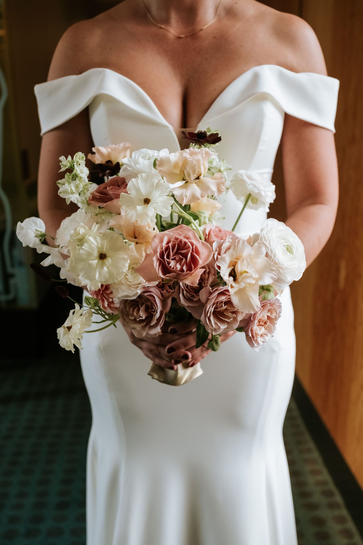 Romantic bridal bouquet with white and dusty pink flowers against white wedding dress.