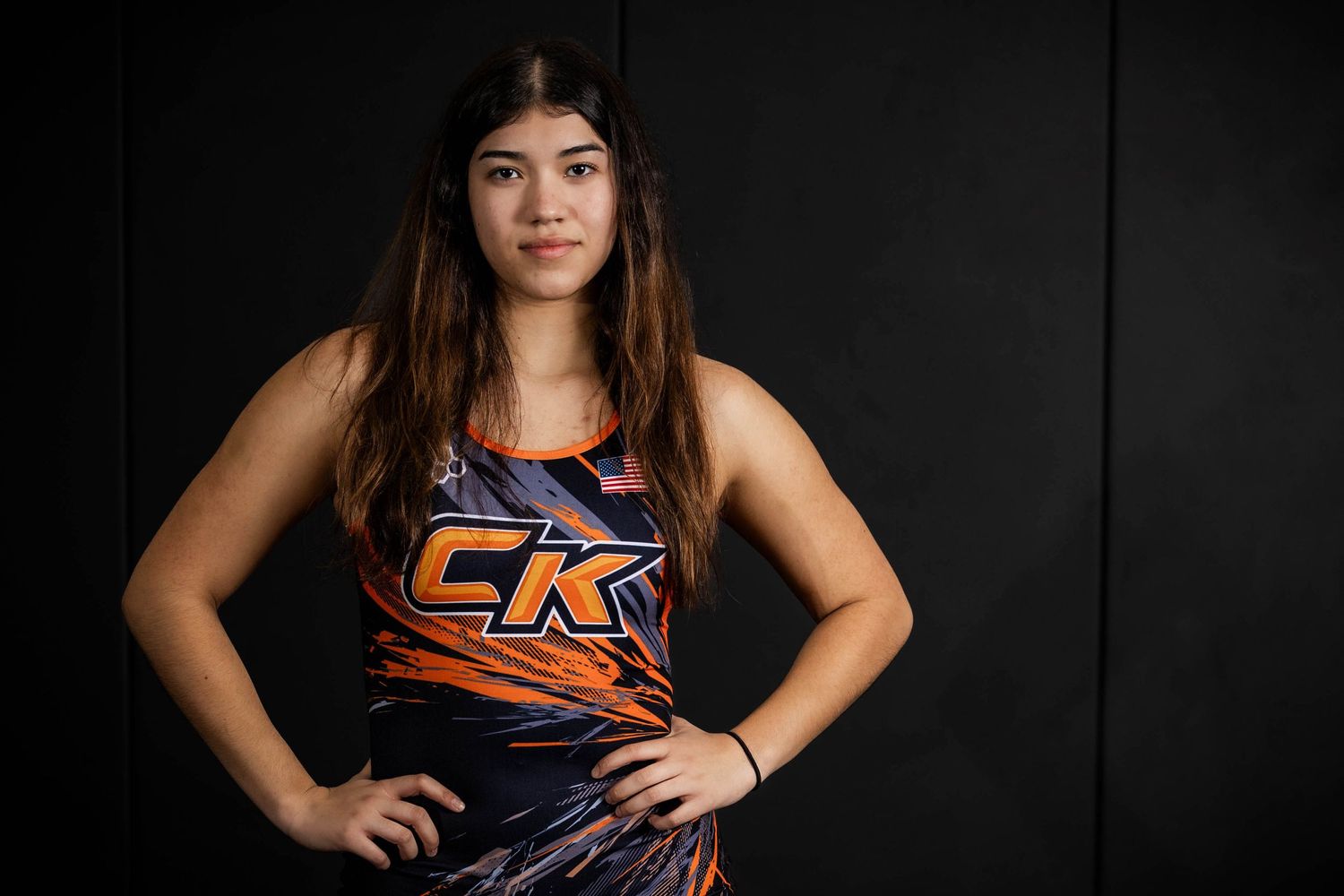 Athletic performer in orange CK tank top poses confidently against dark background in studio portrait.