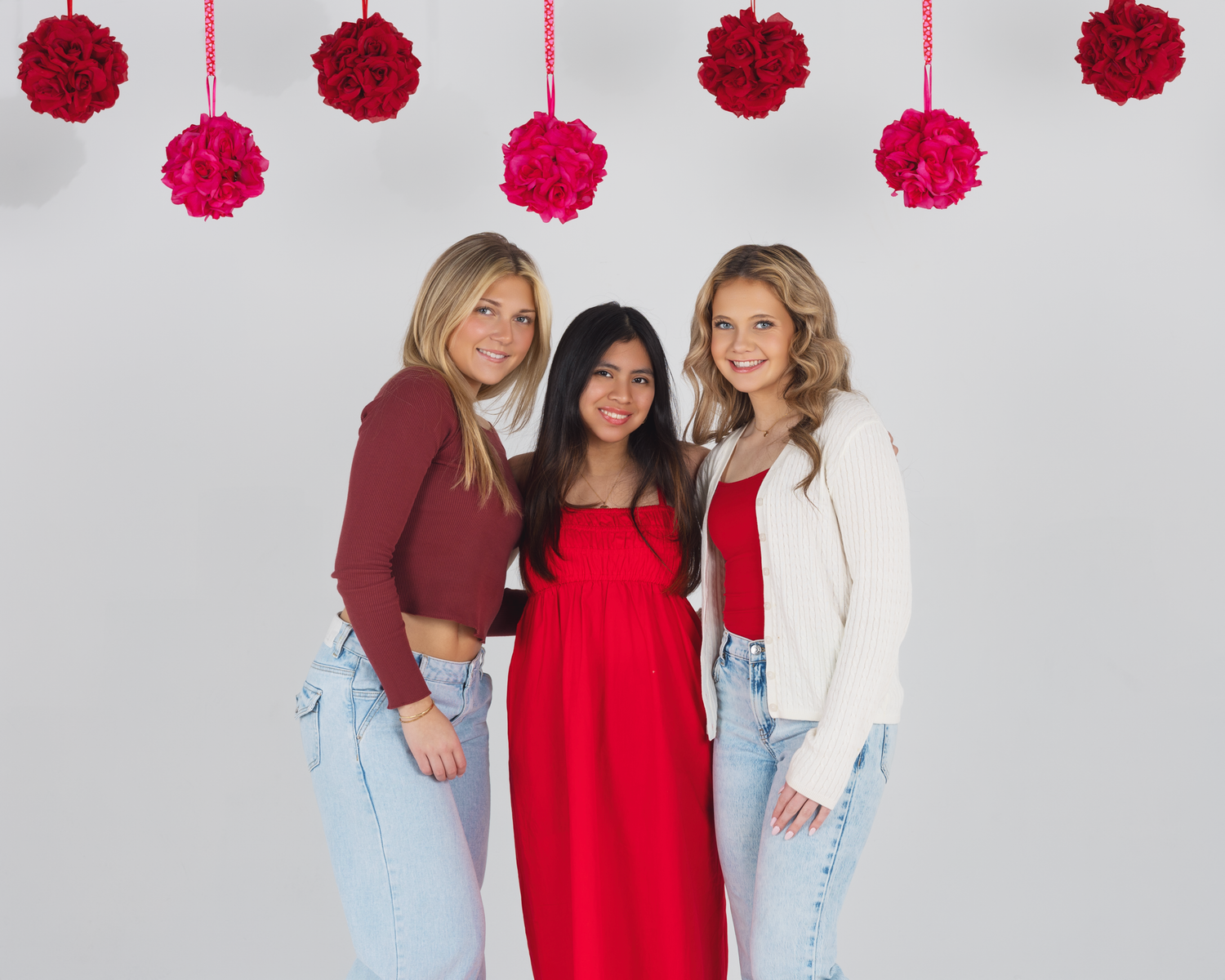 Three TFP model team members pose together against a white background with hanging pink and red pom pom decorations.