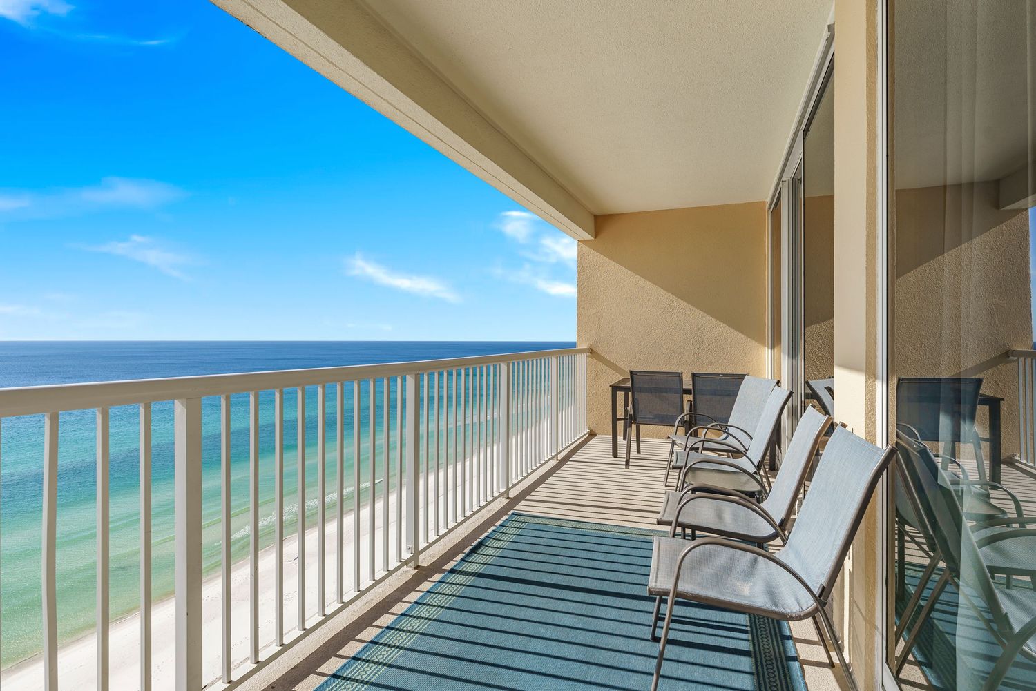 Beachfront balcony with lounge chairs overlooking turquoise waters and white sandy shoreline on a sunny day.