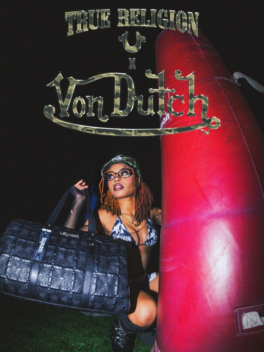 A person in black clothing poses with a large tire in a dark outdoor setting with red lighting effects.