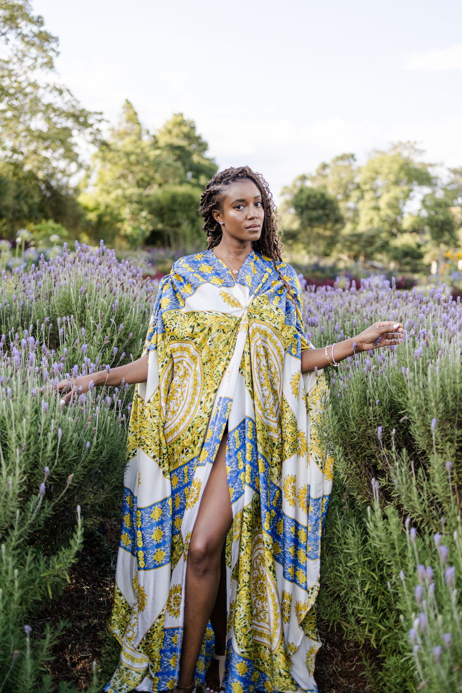 Portrait of a lady standing in lavender field in Naishola Gardens. She has on a blue, green and white kaftan. Ikigu George Photography.
