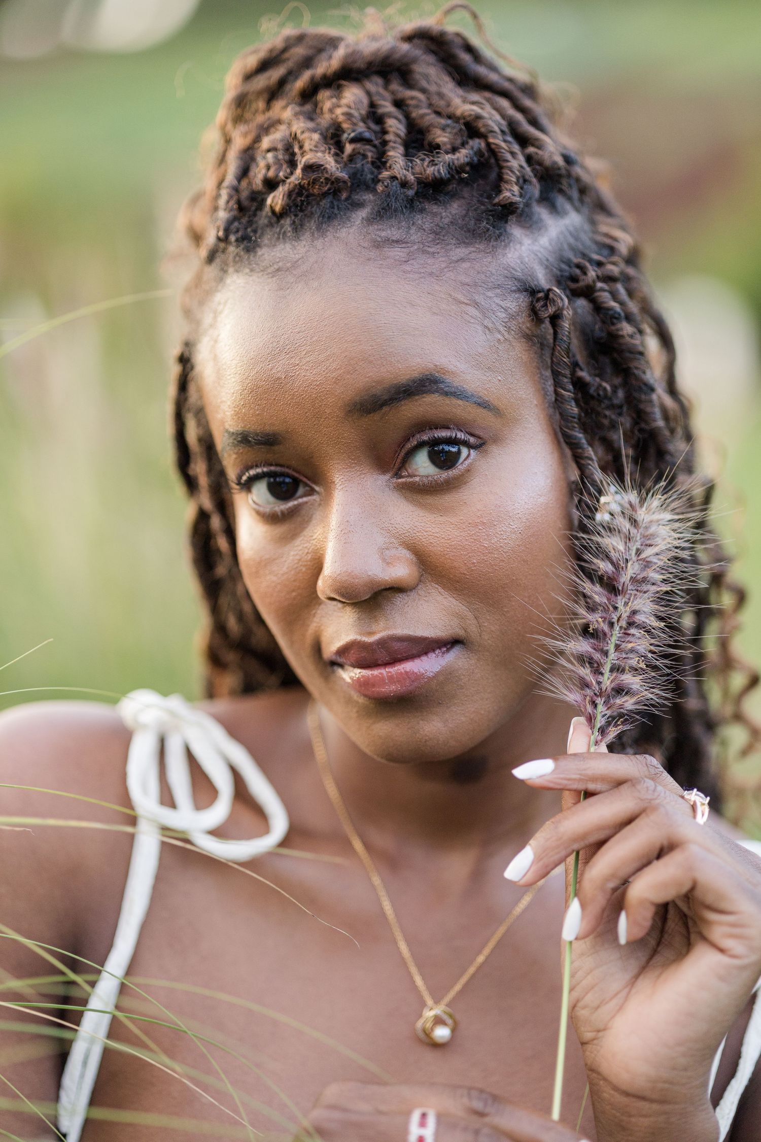 Headshot portrait of a lady in Naiposha Gardens. She's holding a fluffy blade of grass up to her left cheek. Ikigu George Photography.
