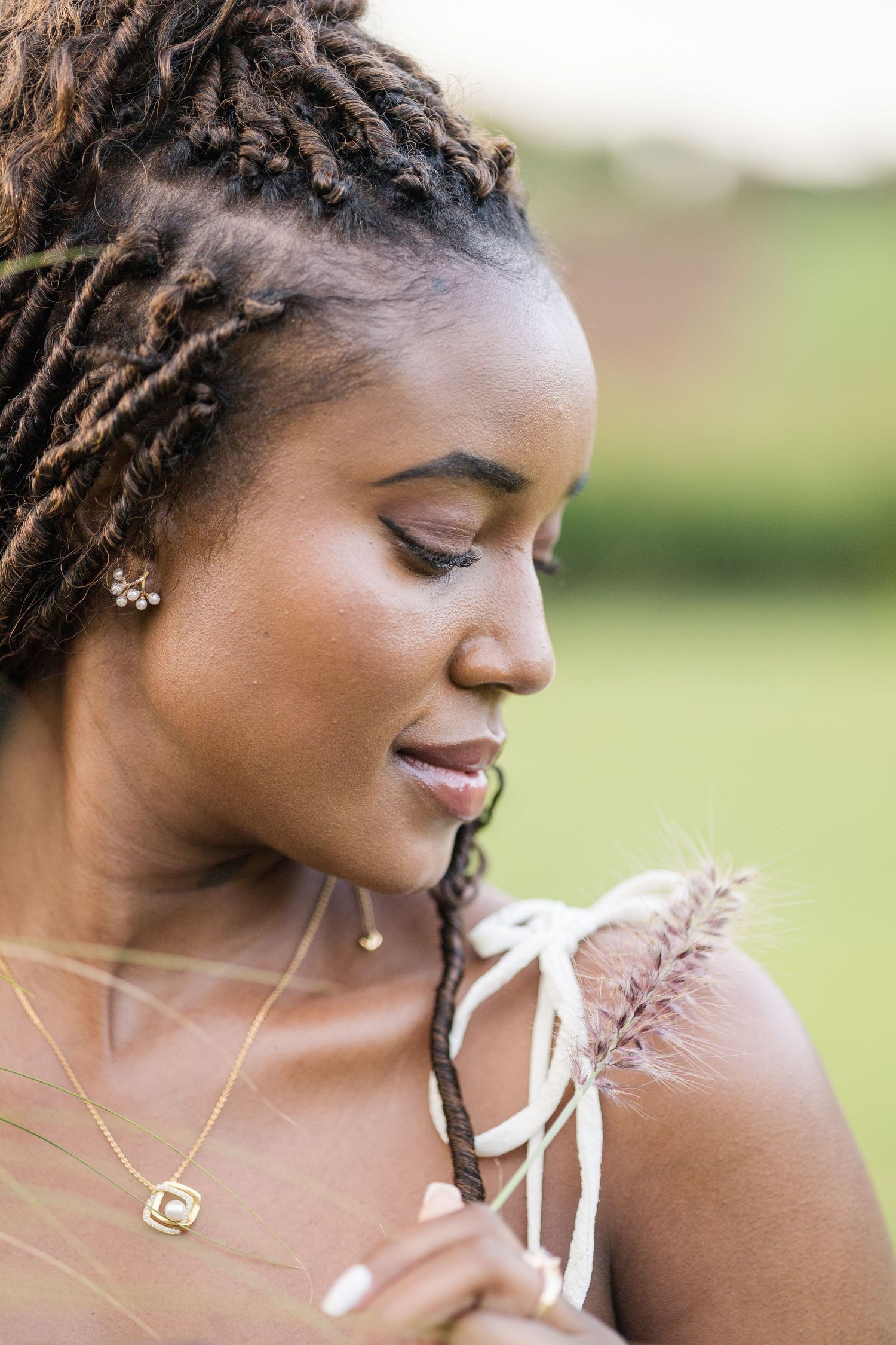 Headshot portrait of a lady in Naiposha Gardens, looking to her left, holding a blade of grass up to her shoulder. Ikigu George Photography.