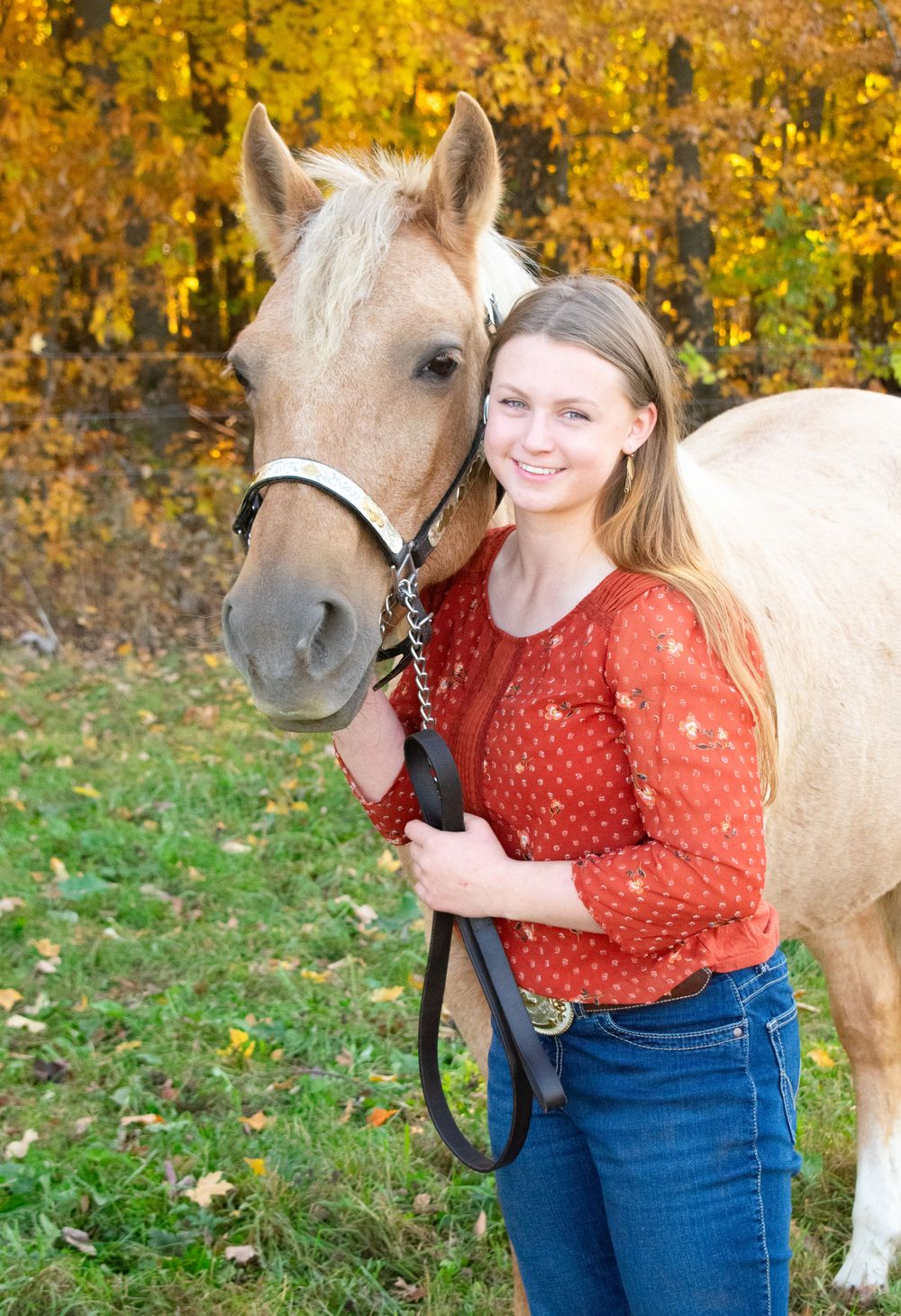 Girl standing next to her horse, smiling at camera in a Wisconsin fall photoshoot.