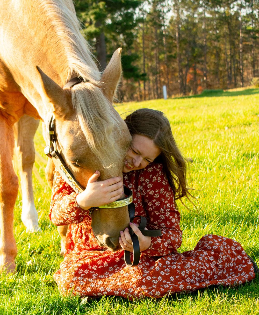 Girl sitting on ground, hugging her horse's face during a Wisconsin fall photoshoot