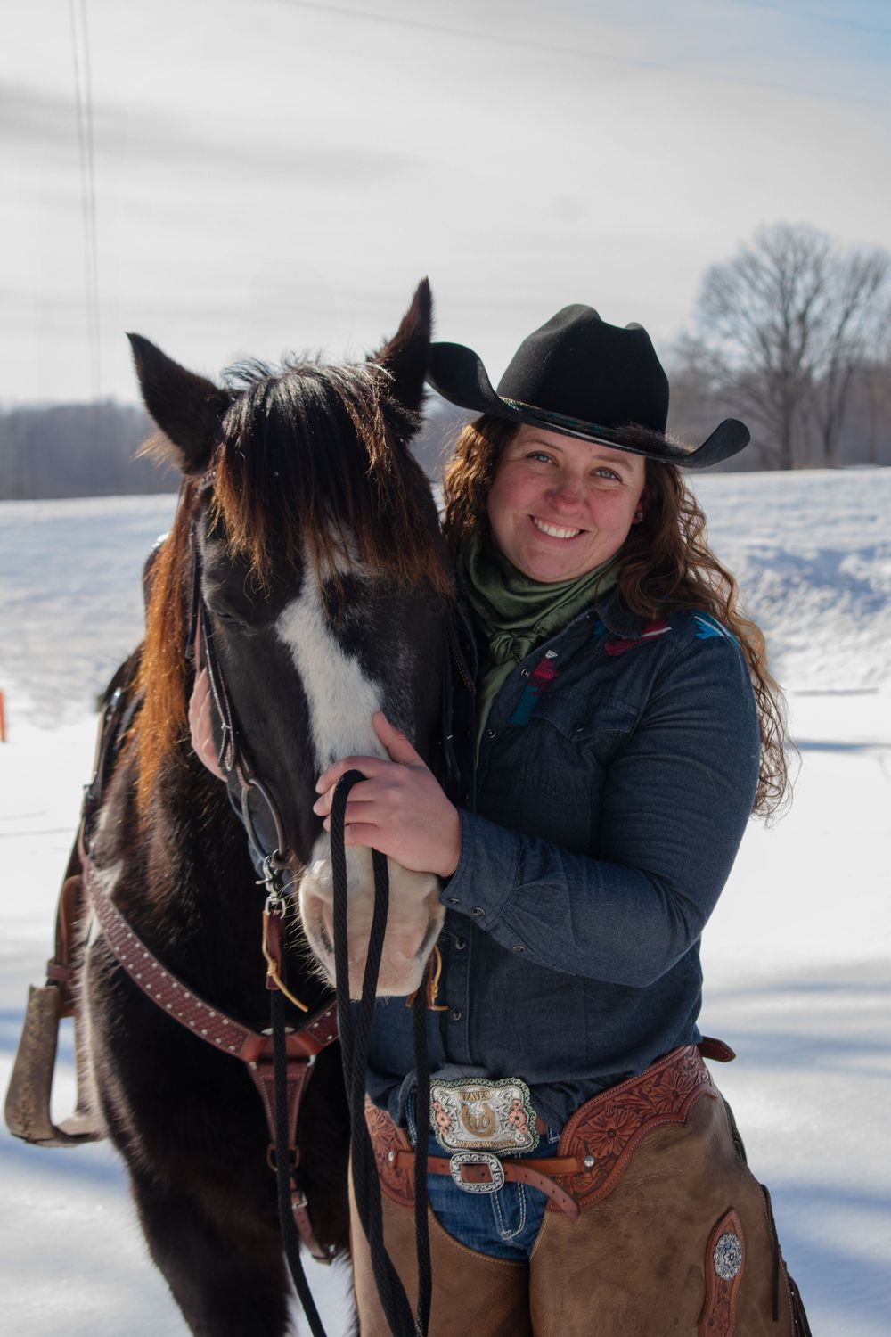 Cowgirl standing with her horse, smiling at camera, in a Wisconsin winter scene