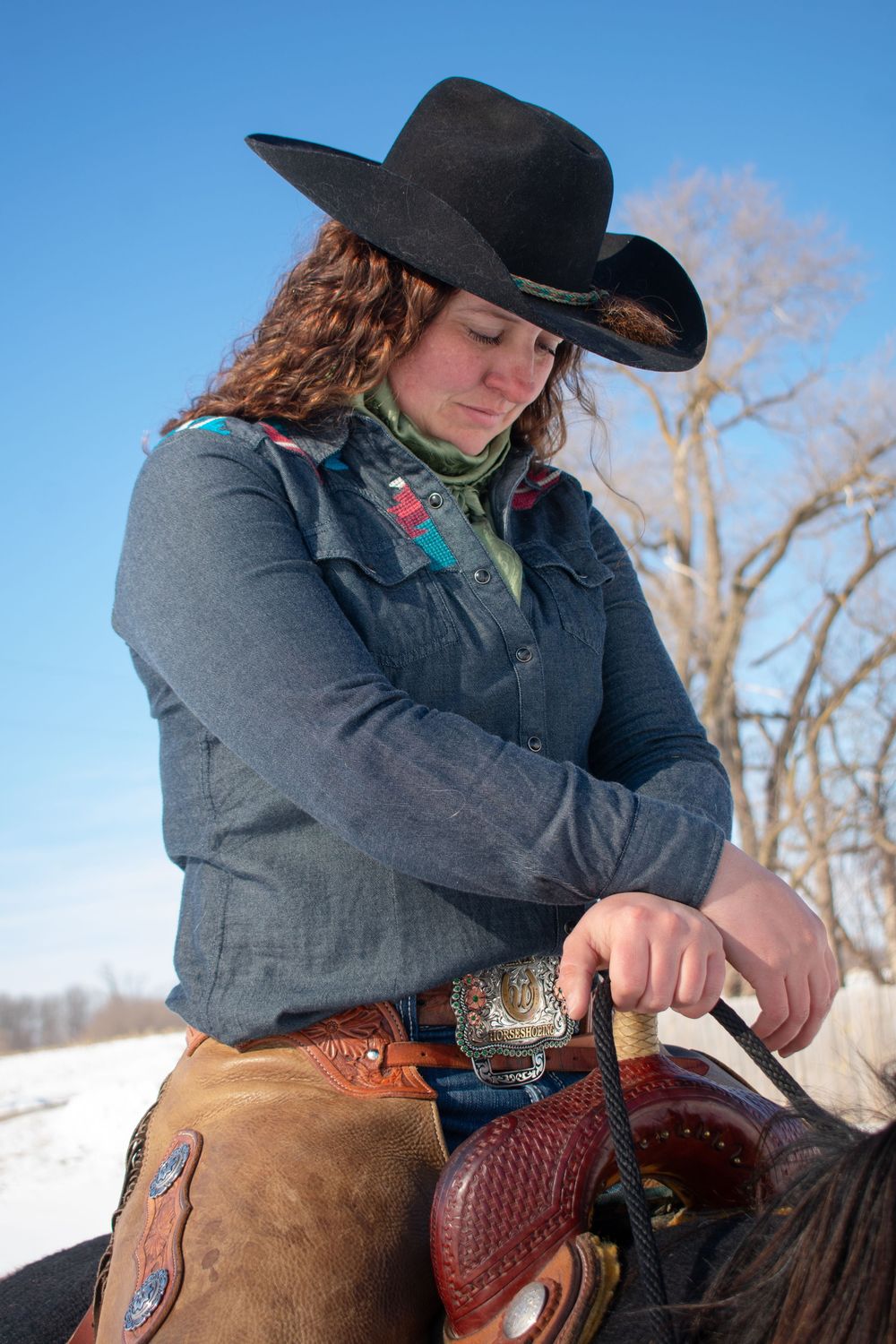 Cowgirl with hands crossed over saddle horn, sitting on her horse looking down in a Wisconsin winter scene