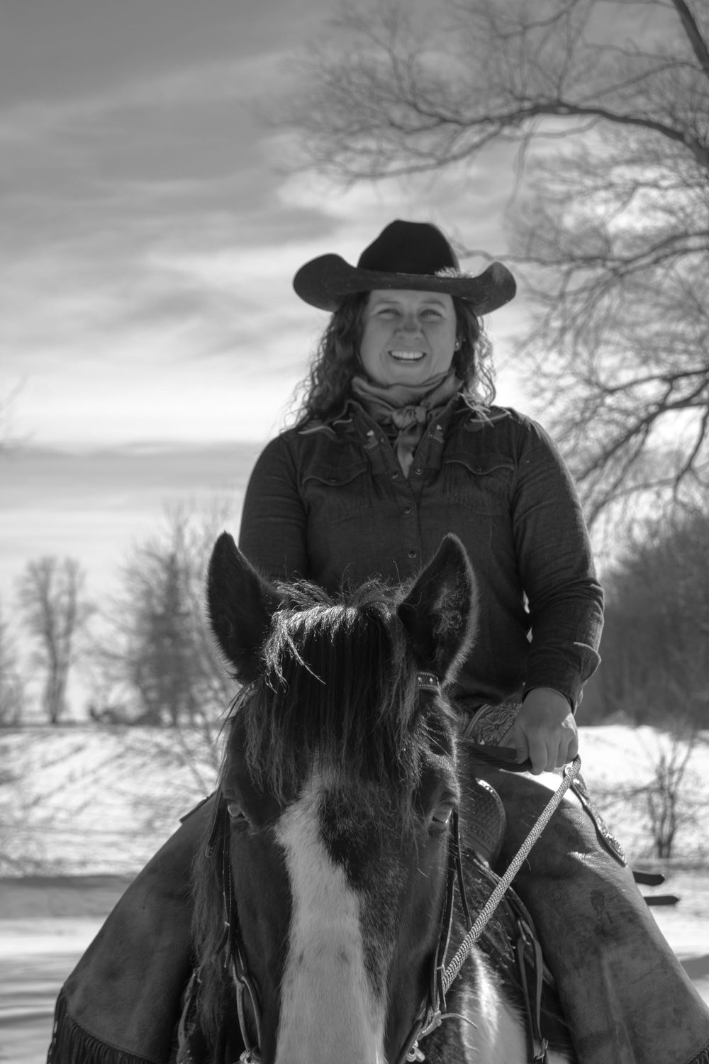 Black and white photo of a cowgirl laughing while riding her horse in a Wisconsin winter scene