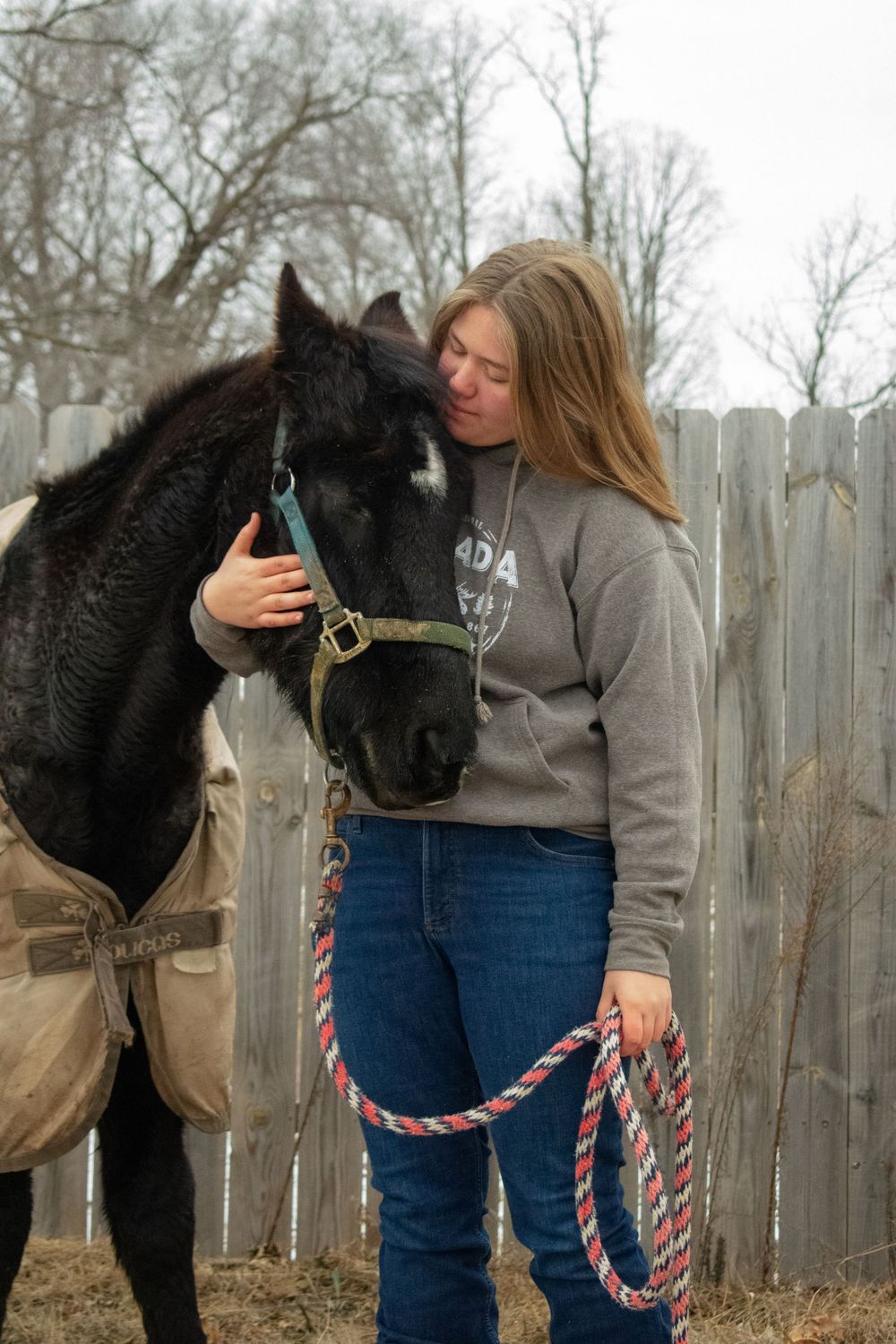 Girl standing with her horse, hugging his face to her body, looking at him fondly.