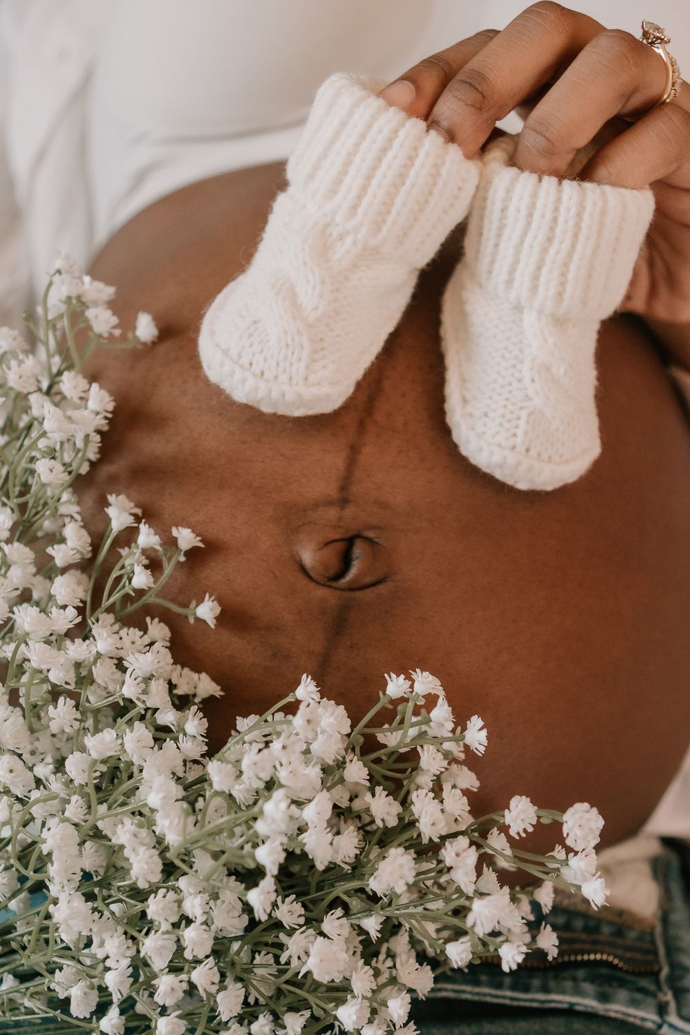 Pregnant belly with tiny white knitted baby booties and delicate white baby's breath flowers in a maternity photo.