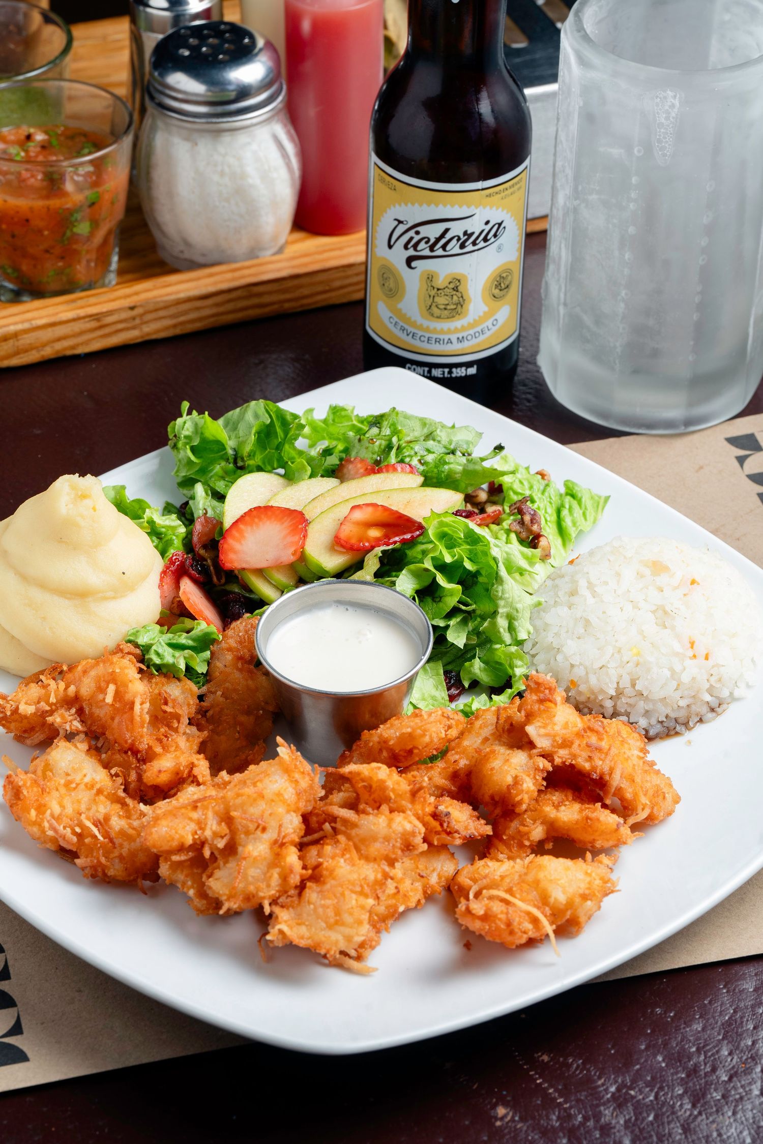 Crispy fried shrimp served with rice, salad and dipping sauce on white plates.
