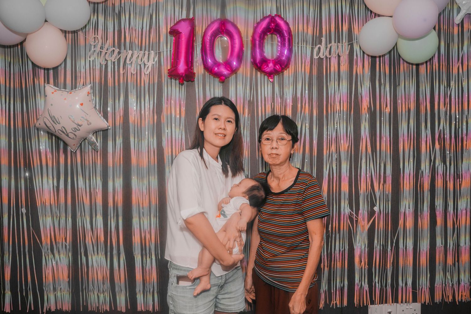 People celebrate a 100 day milestone with pink balloon numbers and silver backdrop decorations.