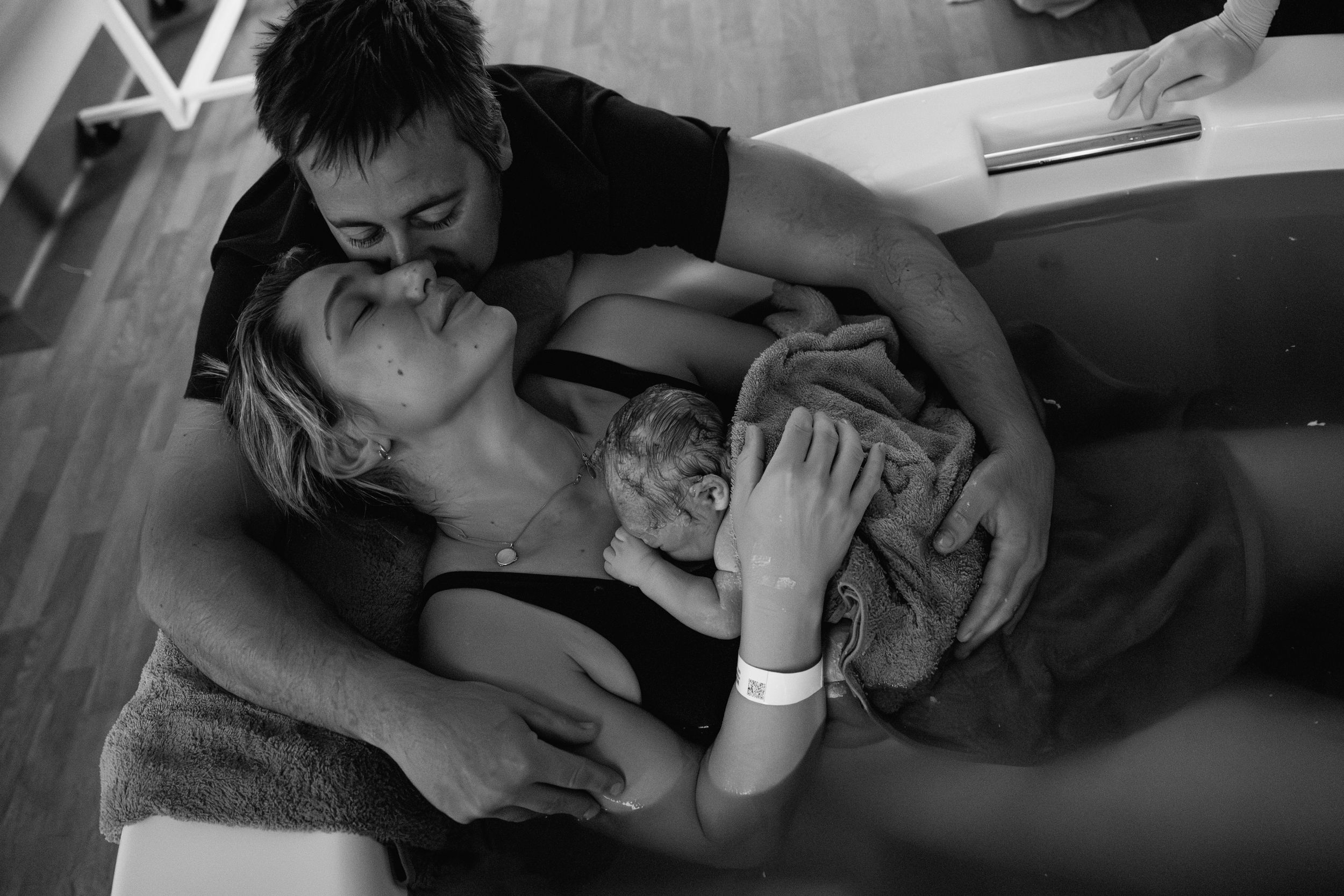 Freshly birthed baby in the birthing tub with mum while dad hugs them both, in Karratha, WA