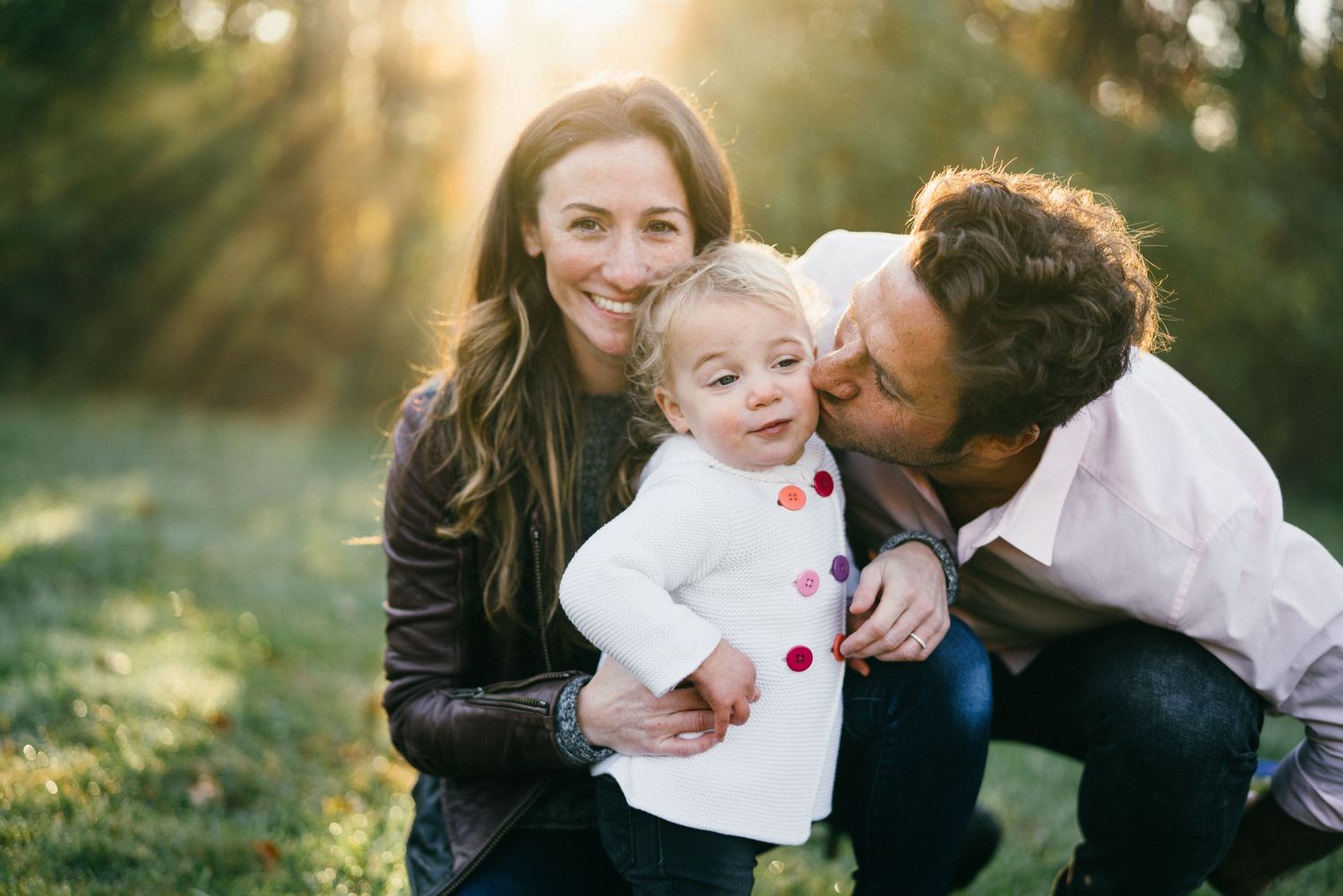 Parents share tender moments with their child in a sunlit outdoor setting during a family photo session.