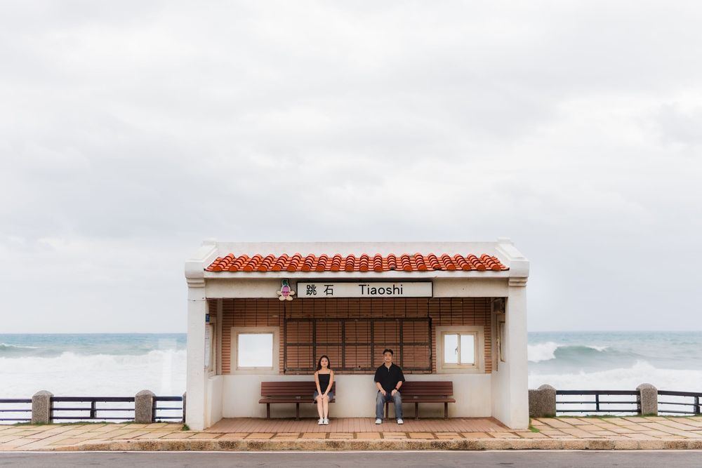 Minimalist beachfront shelter with terracotta roof and wooden benches overlooking the ocean on a cloudy day.