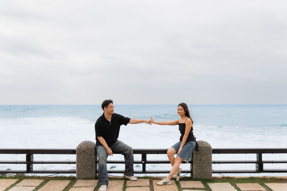 A couple shares a playful moment sitting on a bench overlooking the ocean.