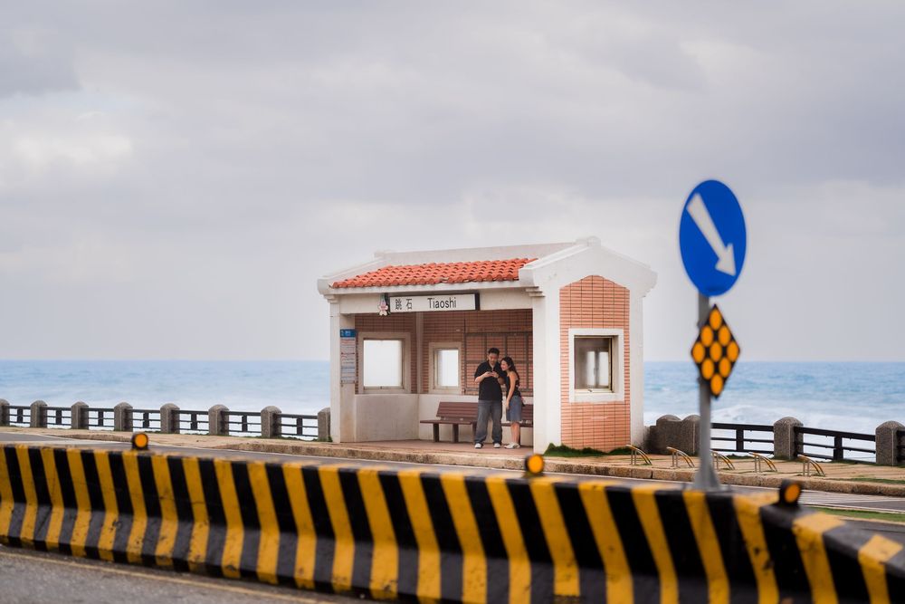 A scenic coastal walkway with benches and railings overlooking the ocean under cloudy skies.