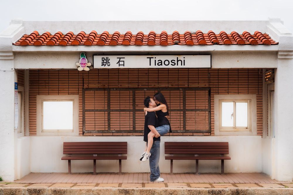 Two people share a romantic moment at the Tiaoshi train station stop with traditional red tile roof in Taiwan.