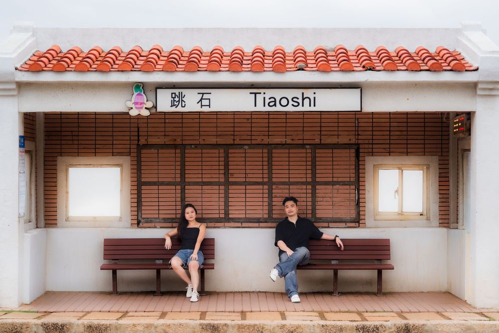A covered waiting area with wooden benches at a train station platform with terracotta roof tiles.