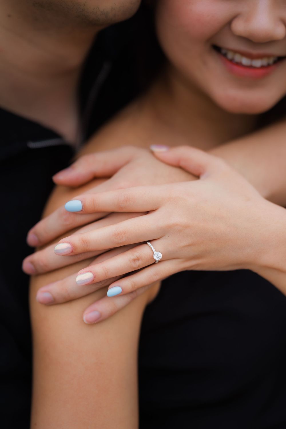 Close-up of hands showing off an engagement ring with light blue and neutral manicured nails.