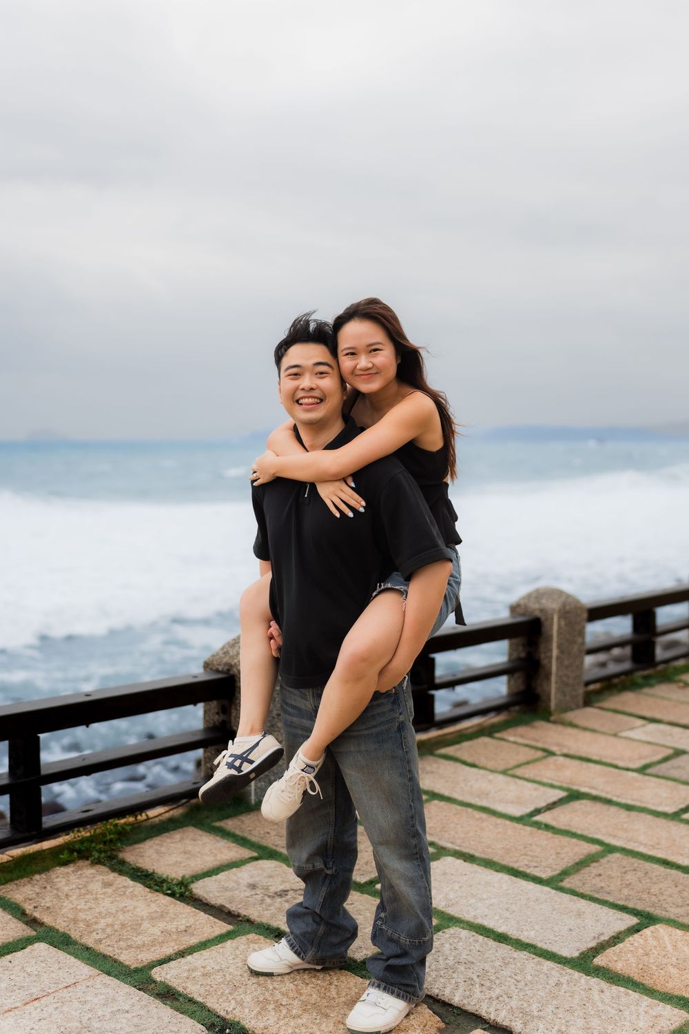 Two people sharing joyful moments and embraces on a scenic overlook with a cloudy backdrop.