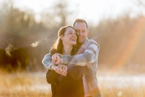 Een winterse locatie met rietgras, waarbij man zijn vrouw vanachter omhelst. Zij lacht over haar schouder. Koude adem is zichtbaar