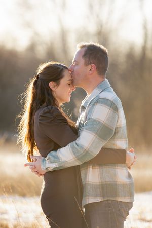 man en vrouw in een omhelzing, waarbij hij haar op haar voorhoofd kust.