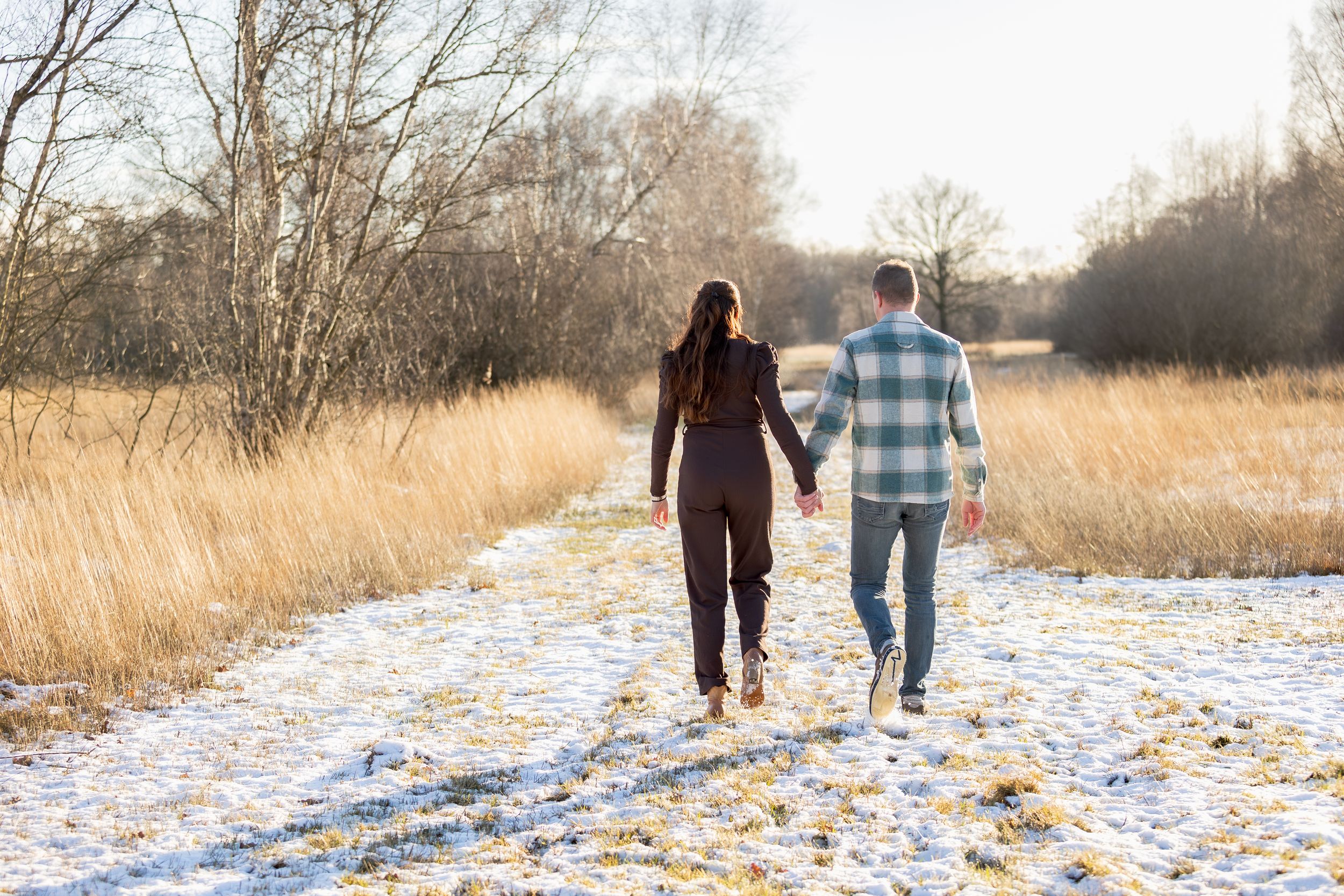 man en vrouw lopen hand in hand door bevroren winterslandschap tijdens een loveshoot