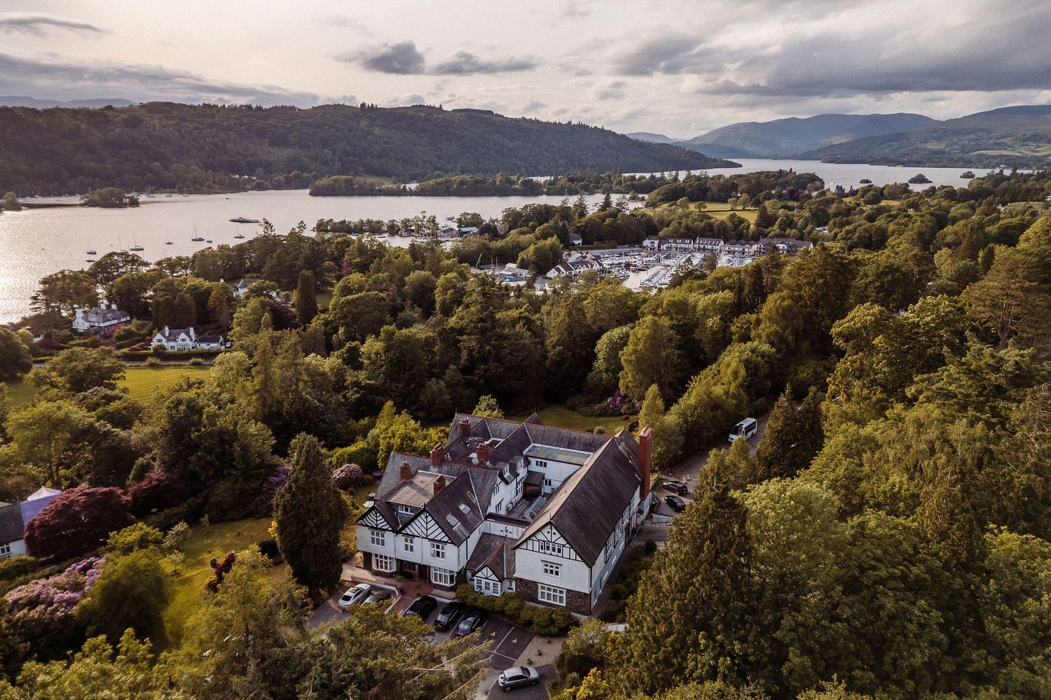 Scenic panoramic view of mountains, lakes, and buildings nestled in a lush green landscape under cloudy skies.