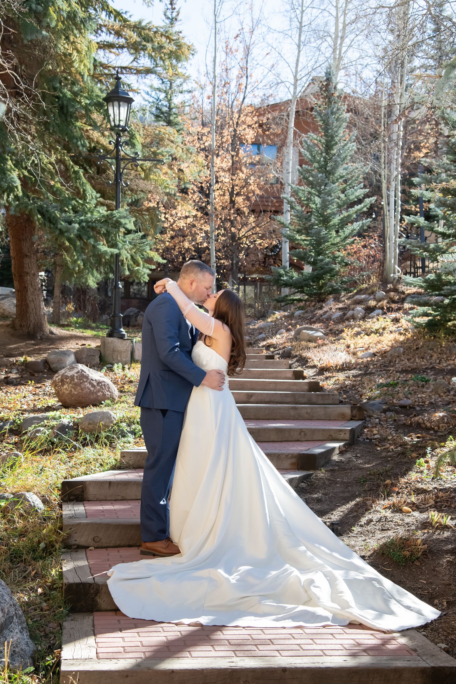 A romantic wedding couple embraces on stone steps surrounded by evergreen trees and autumn foliage in an outdoor setting in Vail Colorado