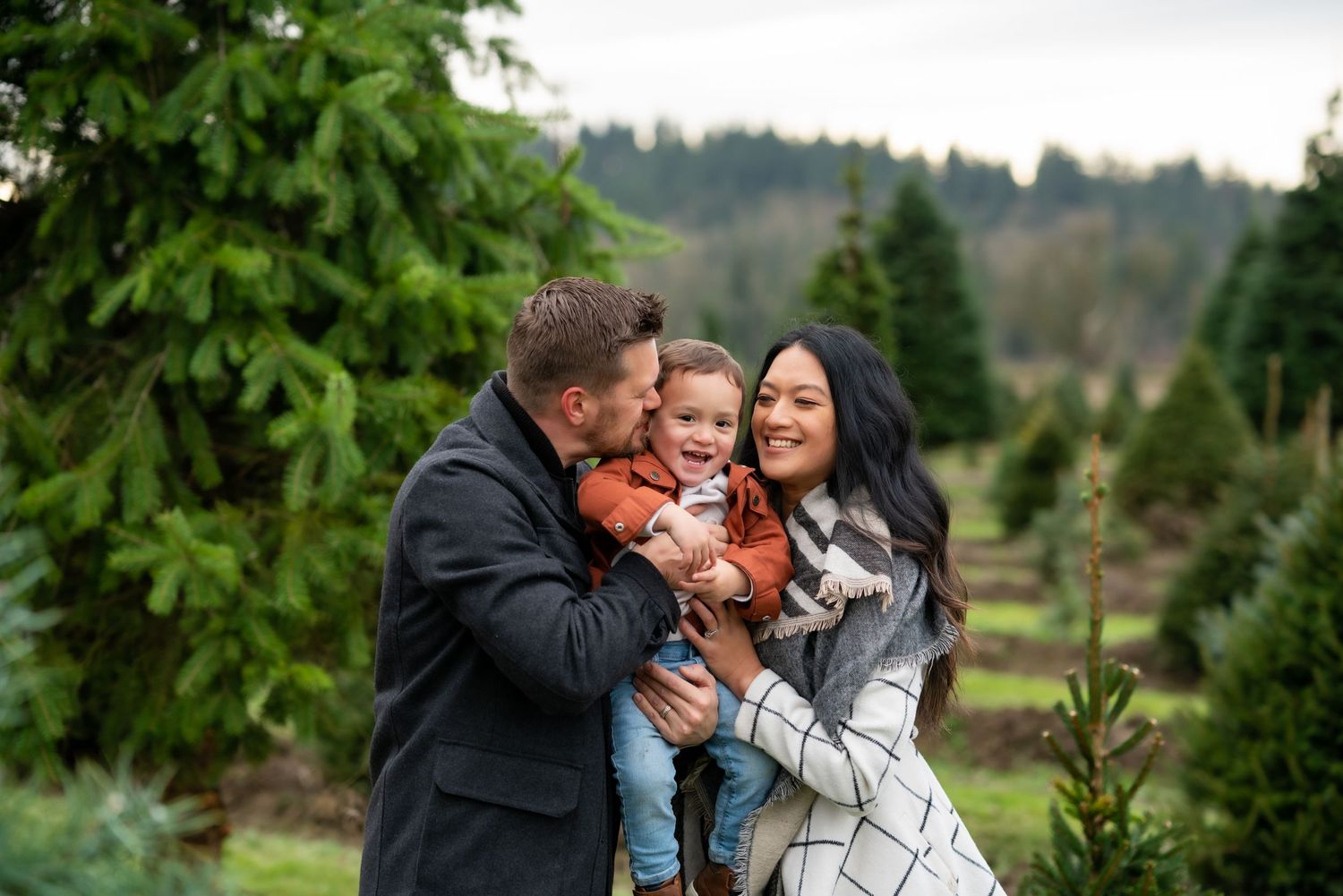 Family embraces outdoors with trees in background at the Campbells Christmas Tree Farm in Snohomish, WA by Filling the Frame Photography.