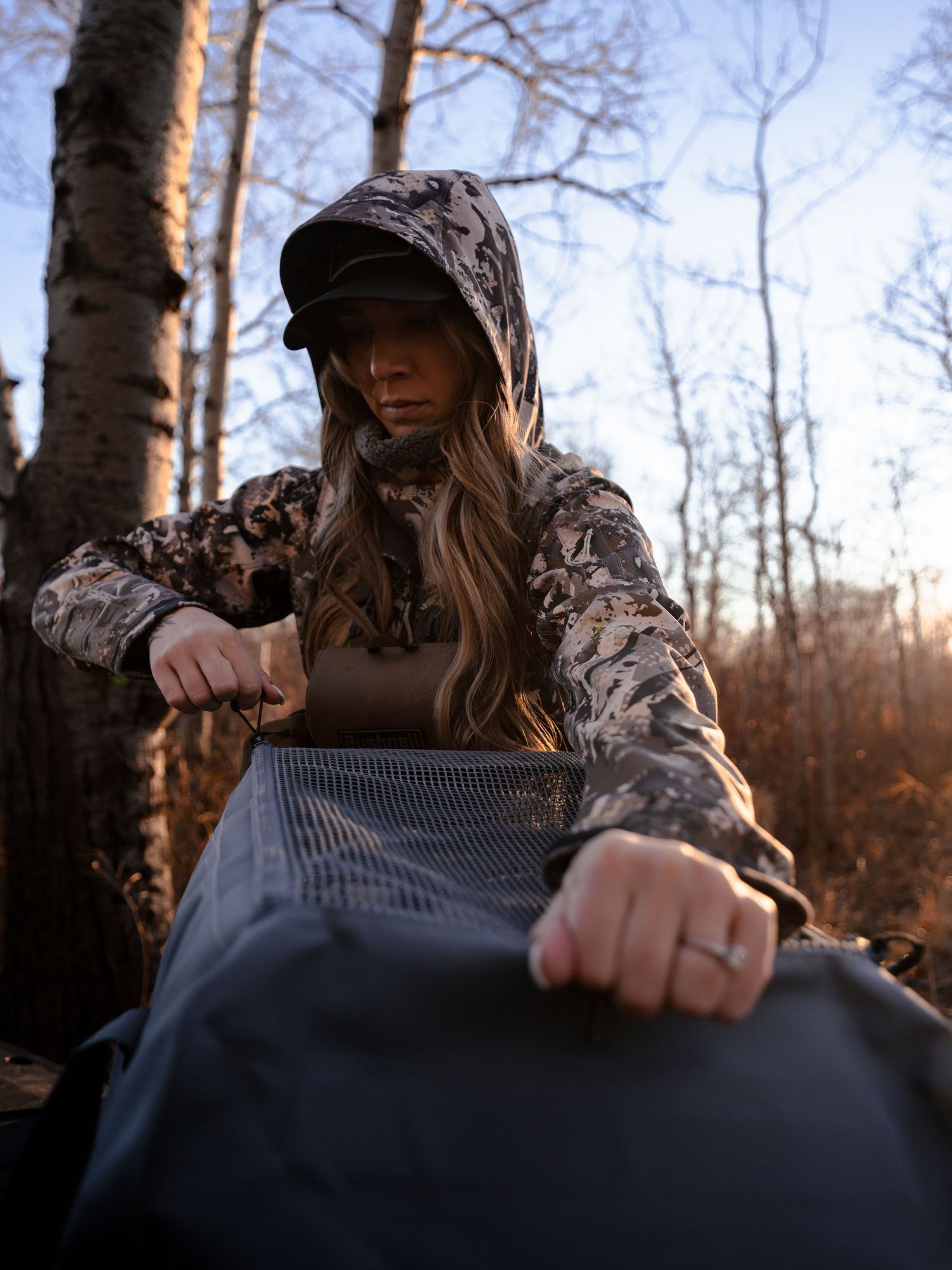 Person in camouflage gear handling outdoor equipment in autumn forest setting.