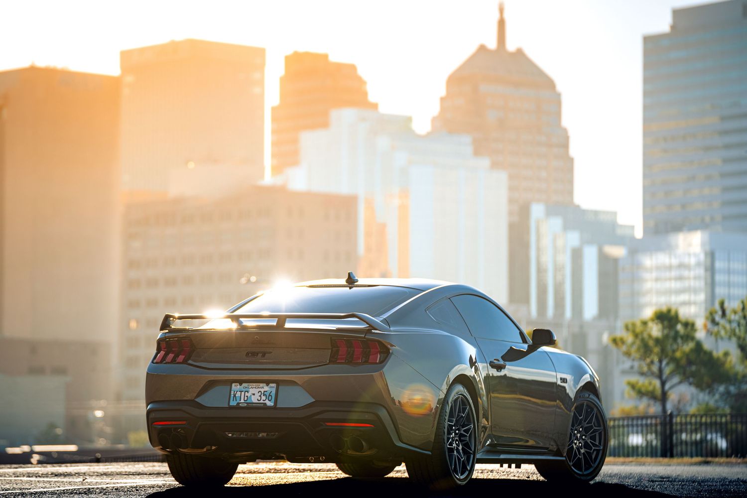 Luxury sports car silhouetted against city skyline during golden sunset with lens flare effect.