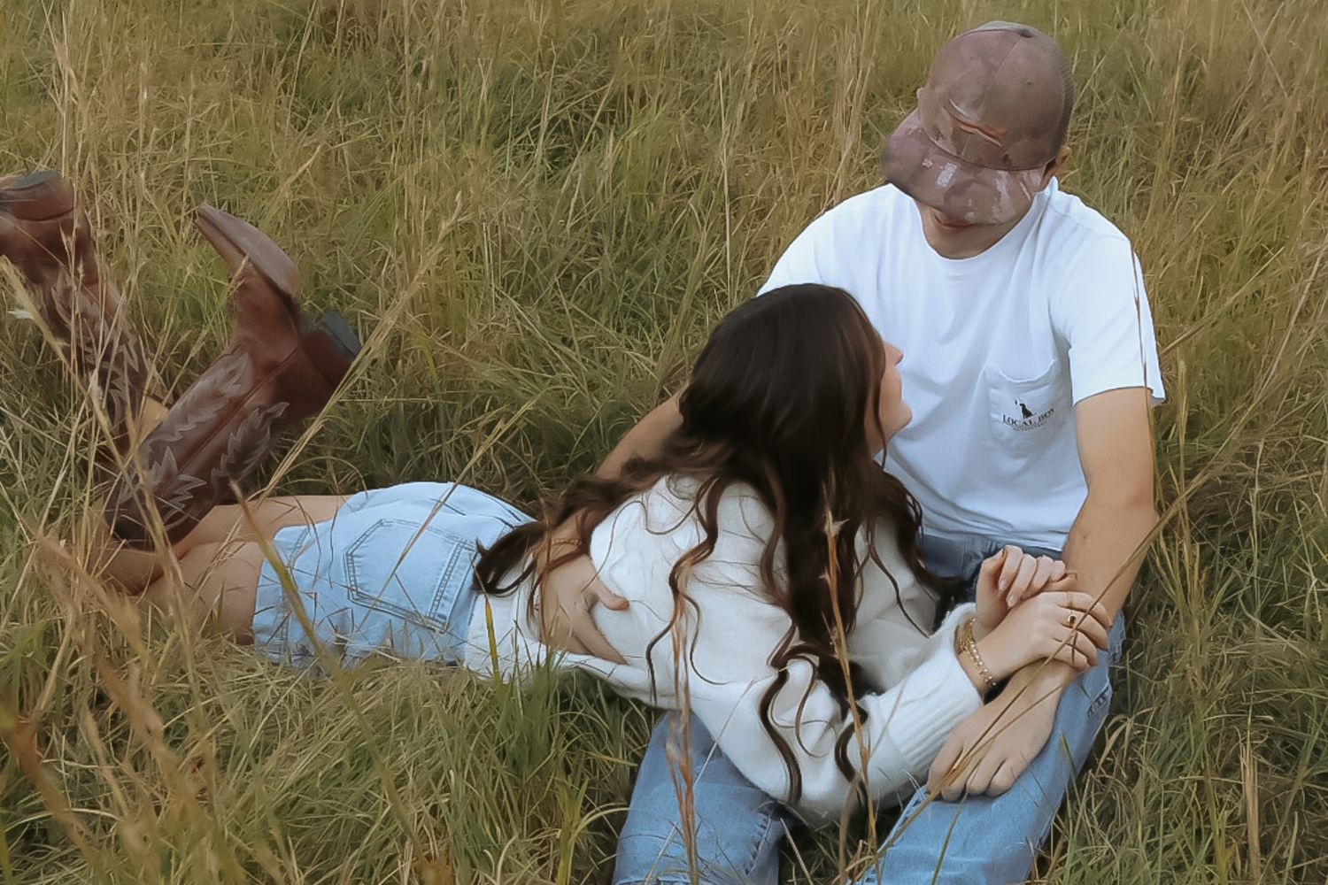 Couple sitting together in tall grass field during golden hour.