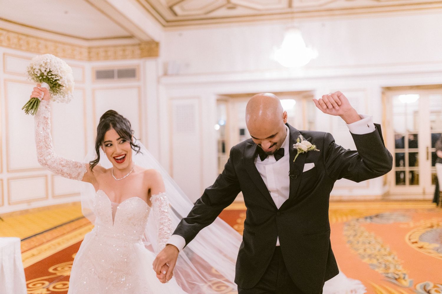 A couple shares a romantic dance in an elegant ballroom with ornate gold trim and white walls.