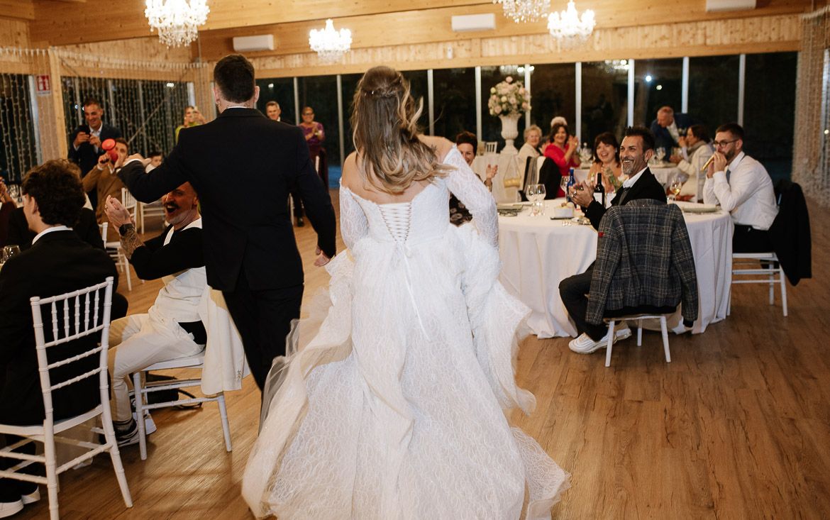 A panoramic view of an elegant wedding reception venue with chandeliers, white chairs and hardwood floors.