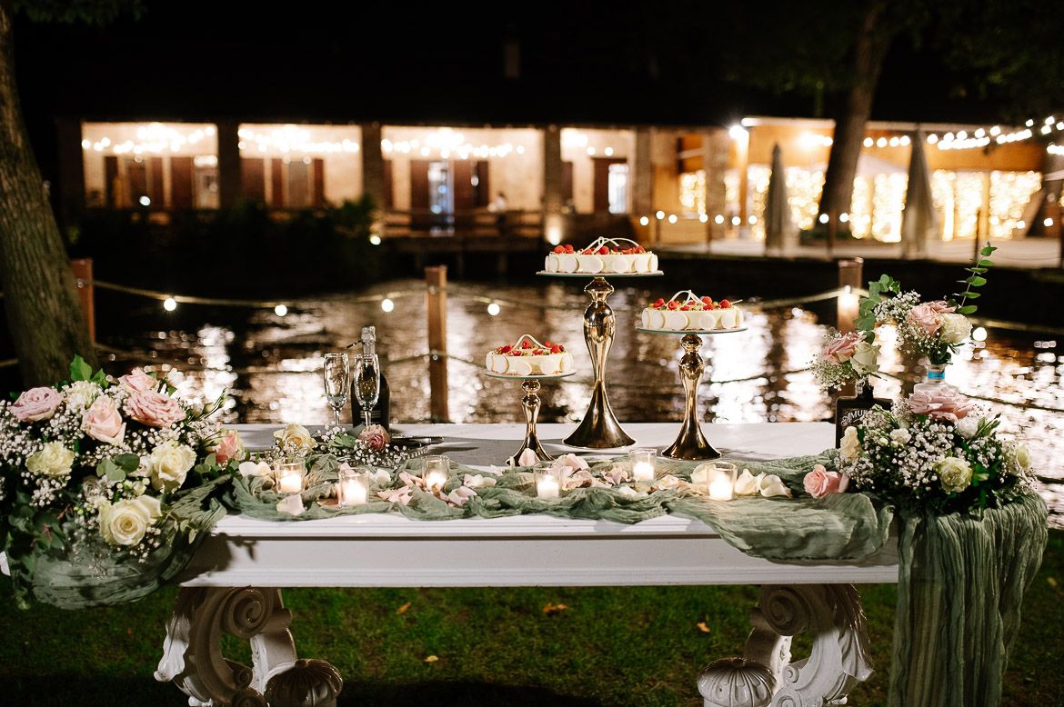 Elegant outdoor wedding reception tables decorated with white linens, greenery and glowing candles at dusk.