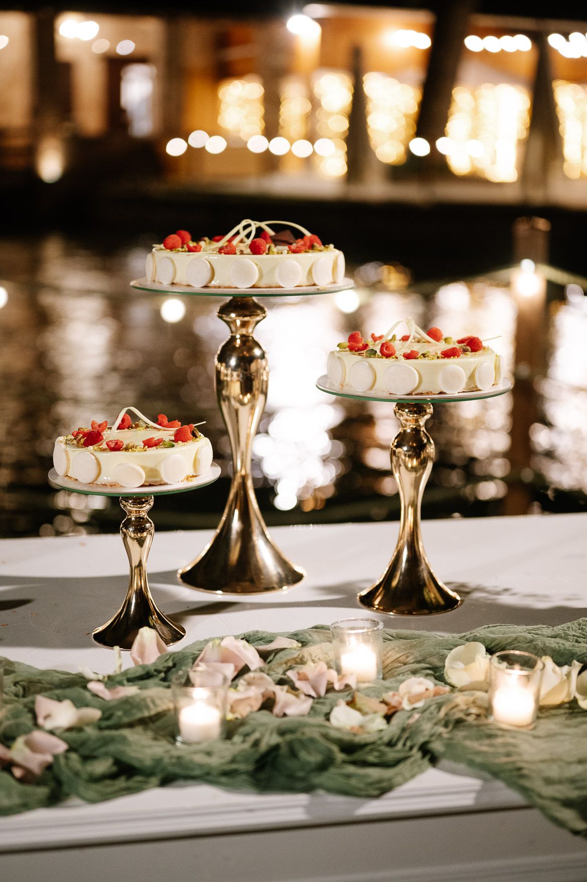Elegant dessert display with tiered cake stands and greenery garland illuminated by candlelight at a wedding reception.