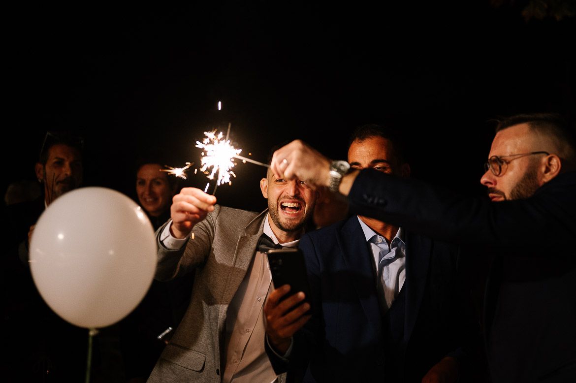 A group of people at a nighttime celebration with sparklers and white balloons creating a festive atmosphere.