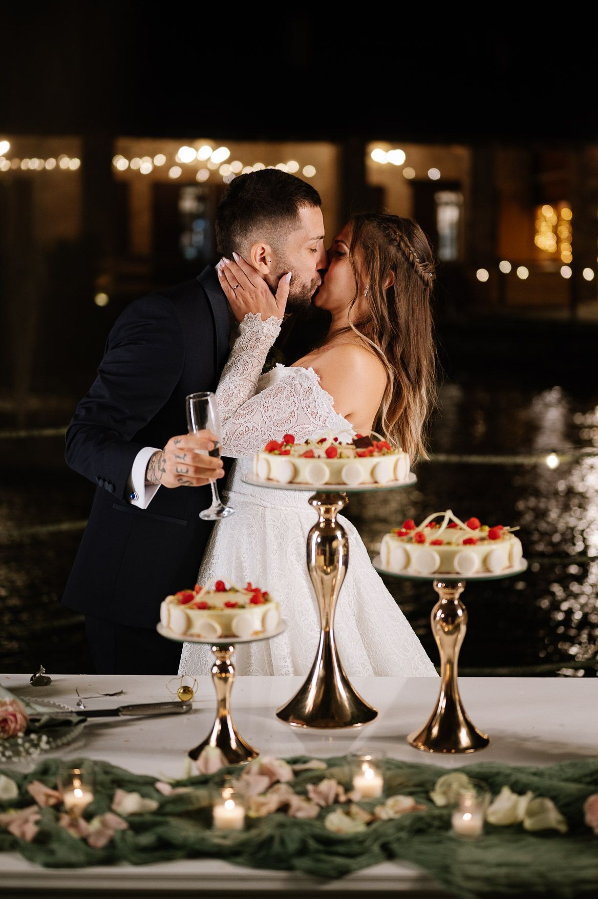 Wedding cake and champagne flutes on an elegantly decorated table with greenery and candlelight.