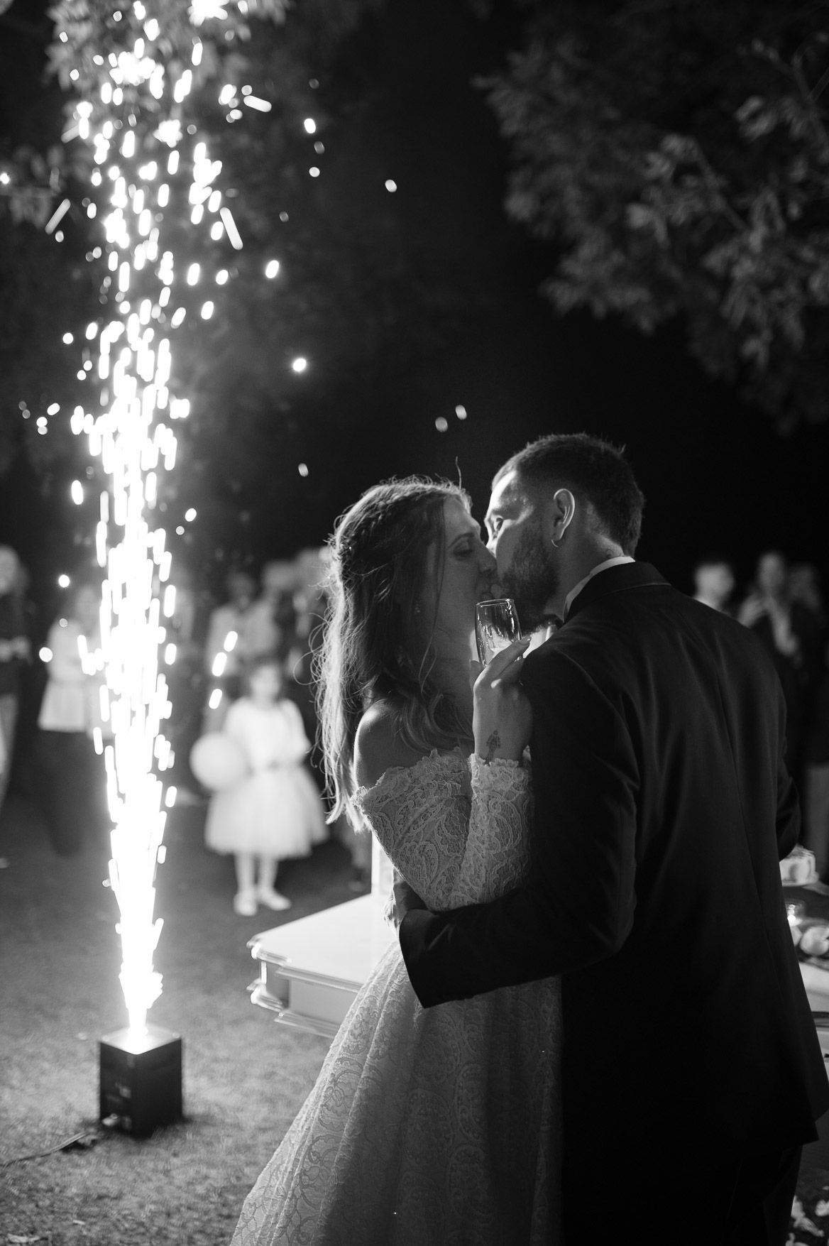 A black and white wedding photo sequence showing a couple embracing with sparklers creating magical light effects in the background.