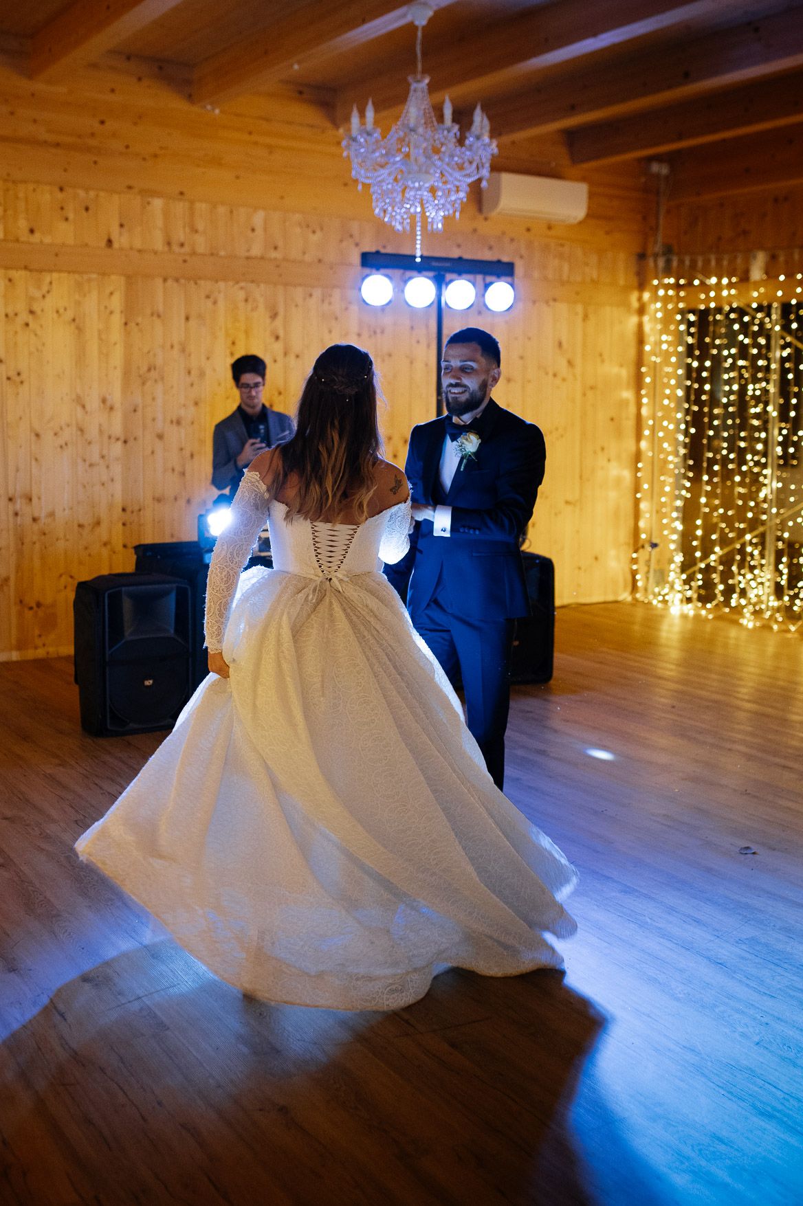A couple dances in a rustic wooden venue decorated with twinkling fairy light curtains.